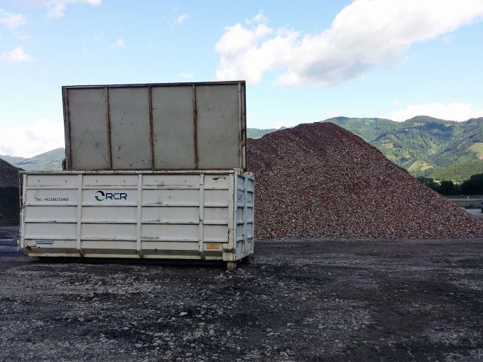 Baucontainer mit Deckel platziert vor einem Schutthaufen des Recycling Center Retznei